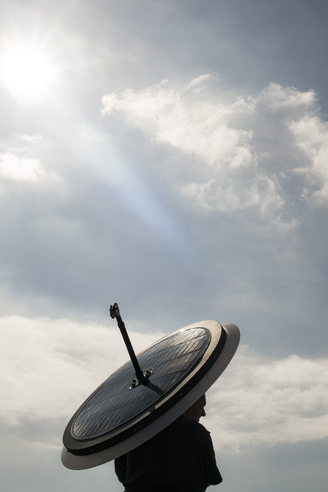 Woman carrying a Sunseeker on her back in front of a beautiful sky with fluffy clouds.